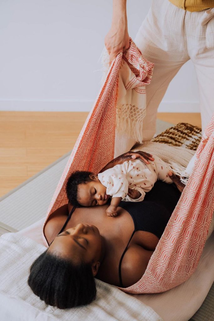 Marisa Bai (doula) pratique un massage Rebozo sur une jeune maman et son bébé.