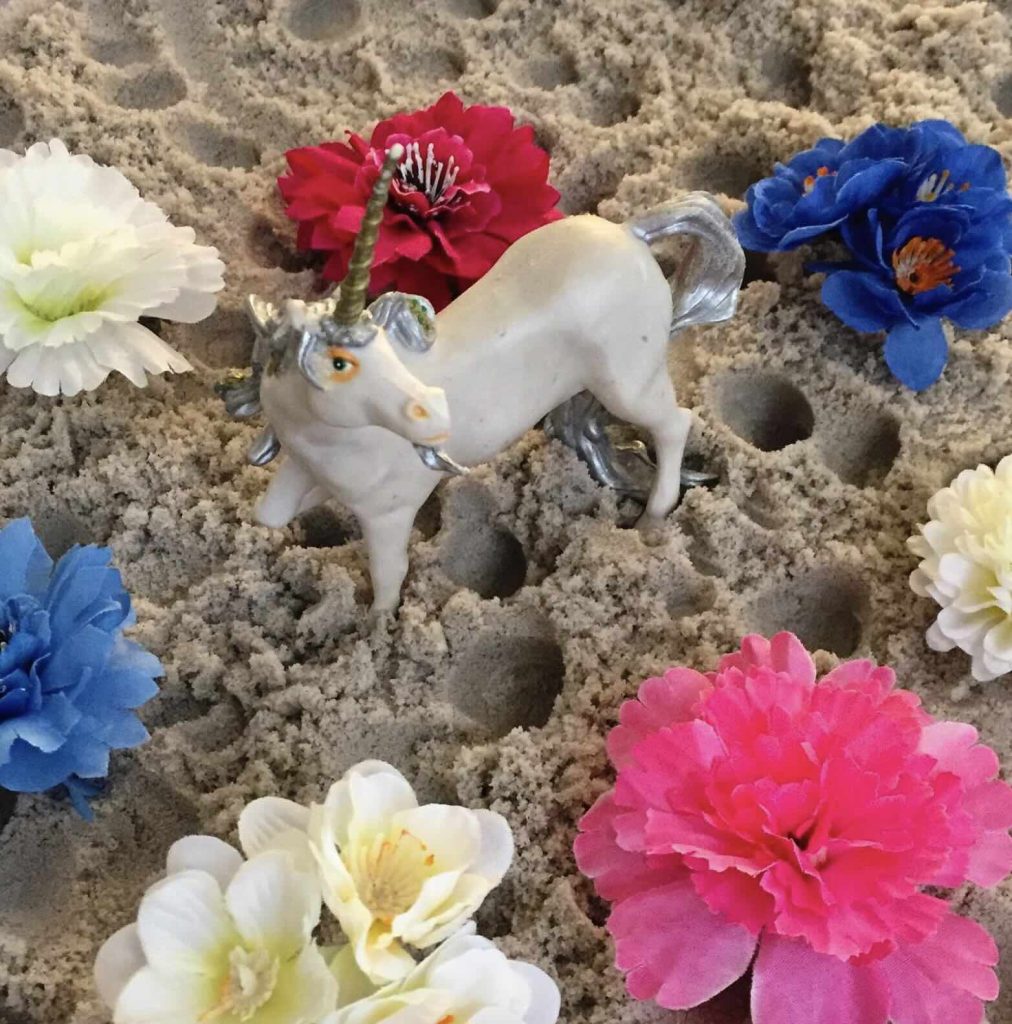 Séance d'une Thérapie par le Jeu de sable : une licorne entourée de fleurs posées sur le sable