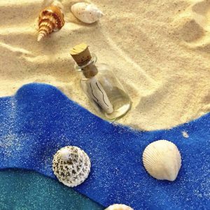 Séance d'une Thérapie par le Jeu de sable : une bouteille renfermant un papier et des coquillages posés sur le sable de couleur doré et bleu