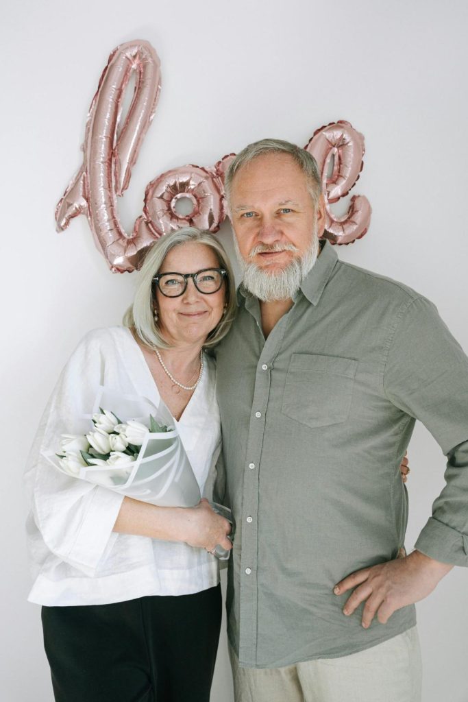 Un homme et une femme âgés posant devant une affiche intitulée Love pour montrer que l'amour peut exister même après 60 ans