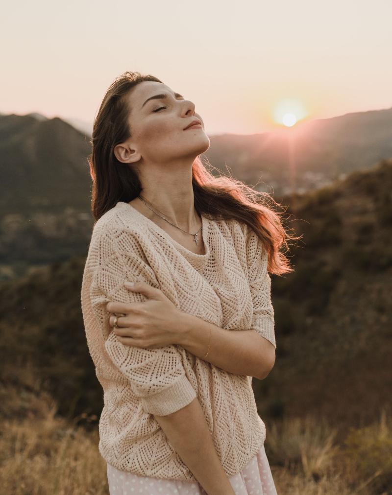 Une femme au petit matin qui a les yeux fermés devant un magnifique paysage et est en posture de gratitude et de ressenti positif dans l'instant présent
